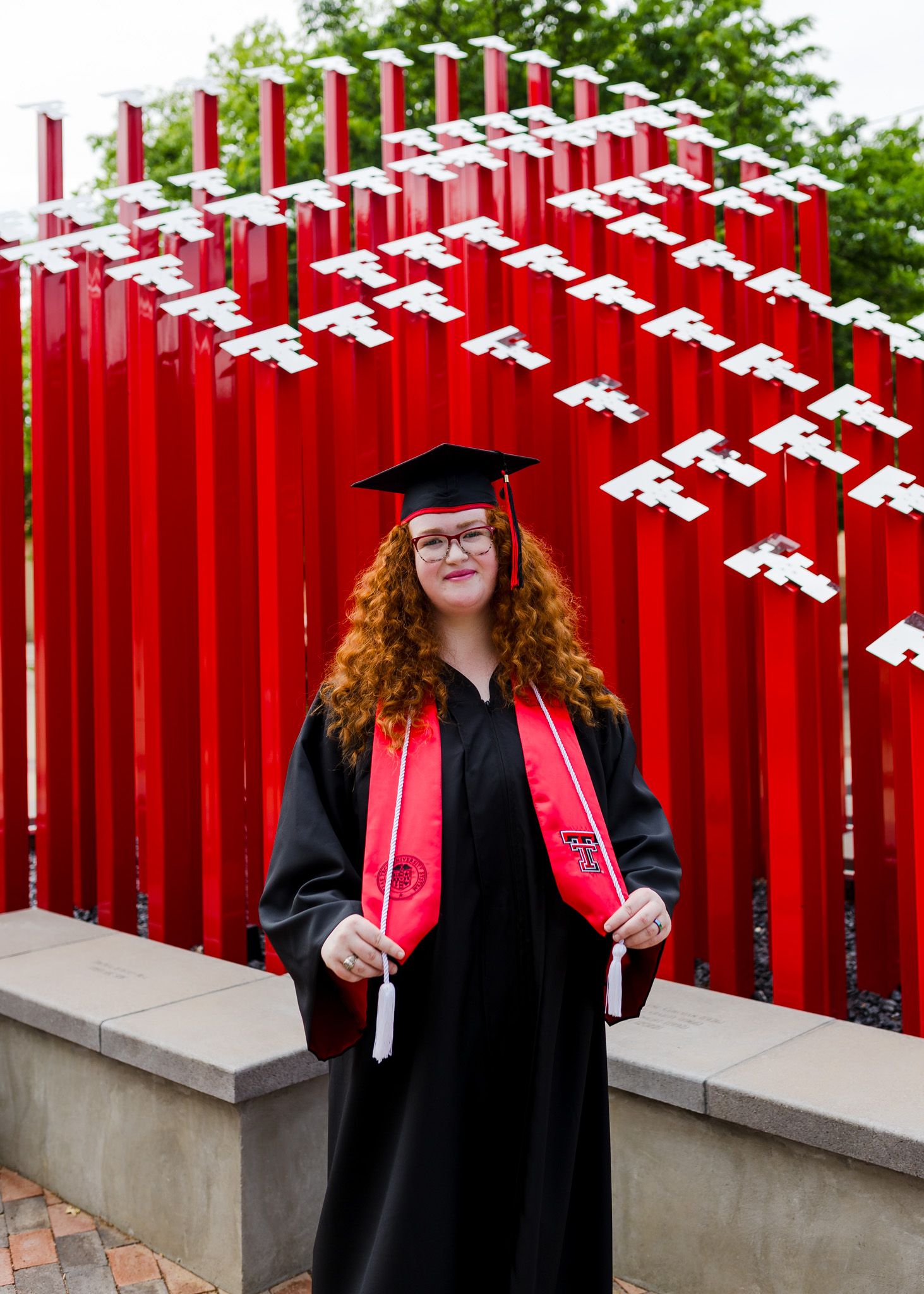 Graduate poses in front of red architectural installation wearing black graduation gown.