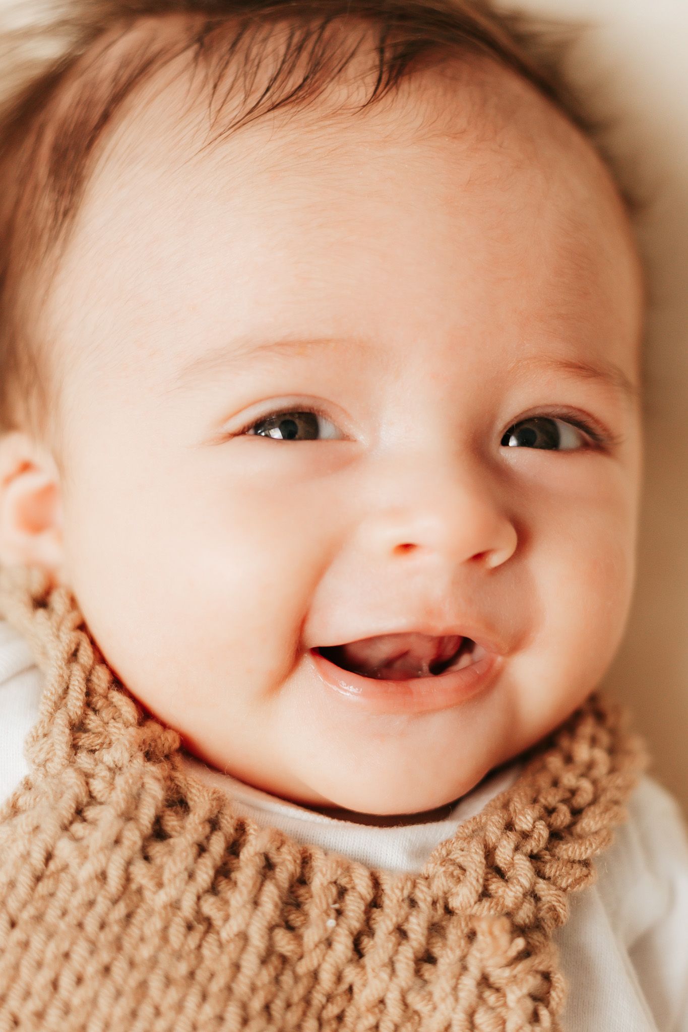 Close up portrait of smiling baby wearing knit beige collar.