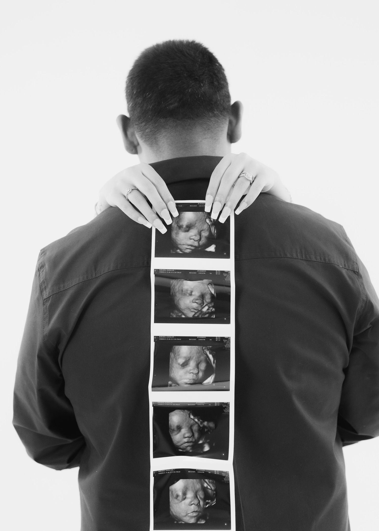 Man holding ultrasound strip against his back in a black and white maternity announcement photo.
