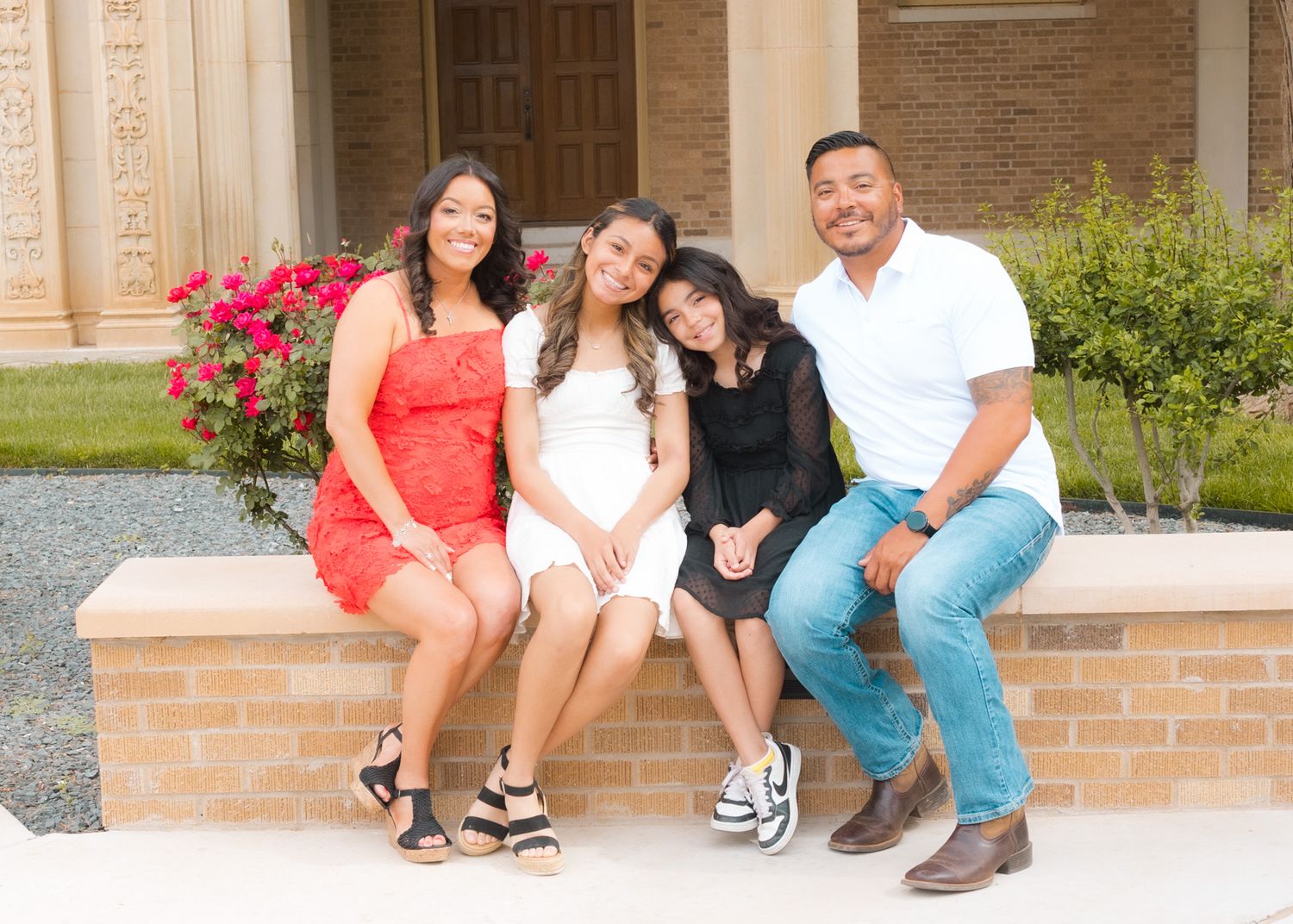 Group sitting together and smiling on brick steps with pink azalea bushes and doors behind them.