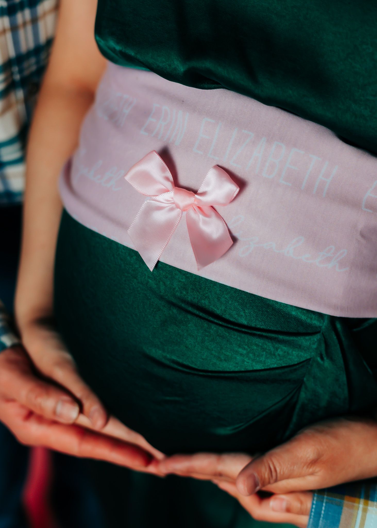 Pink sash with bow detail wrapped around a dark green maternity dress.