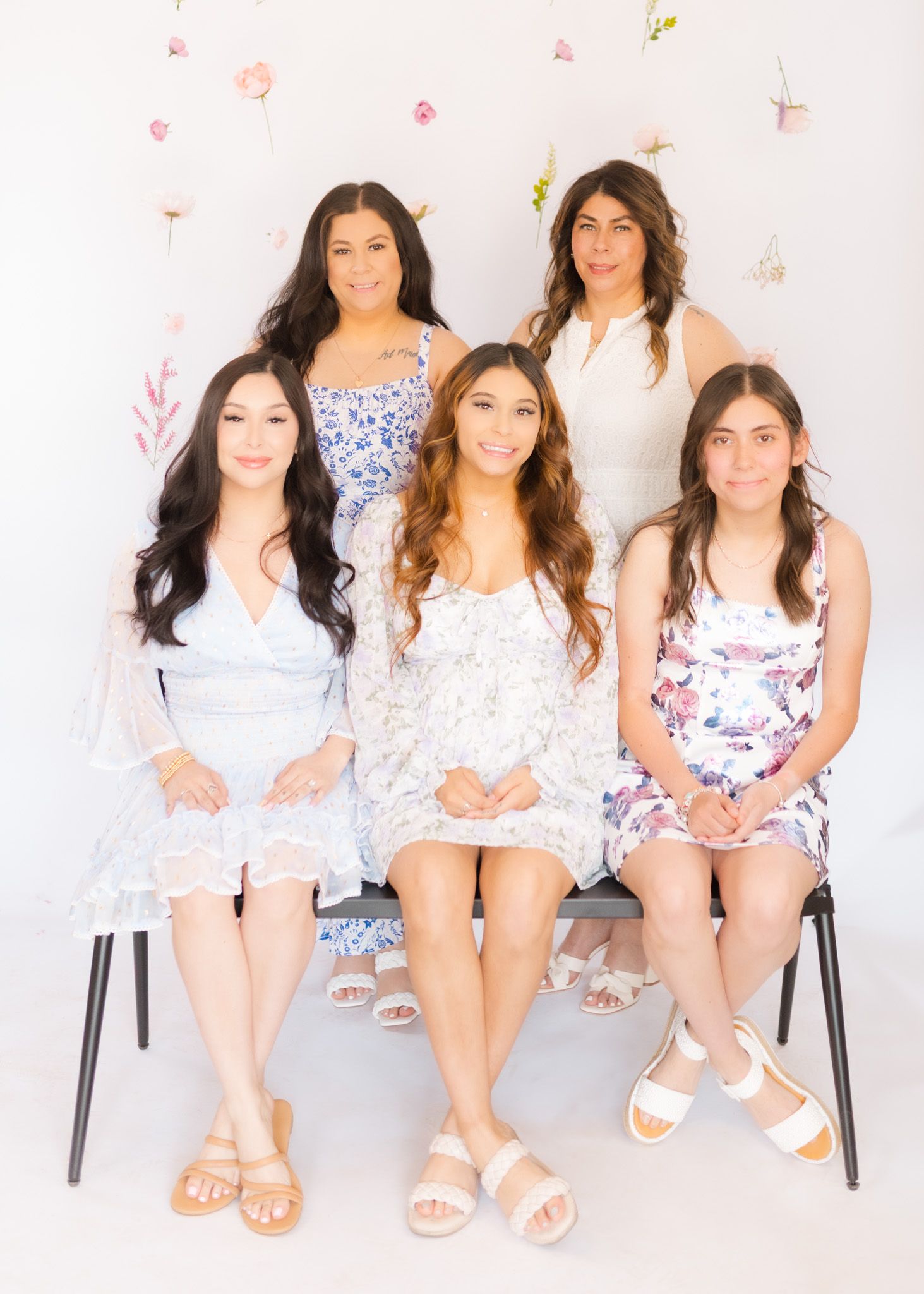 Group photo with five people in white floral dresses against decorated background.