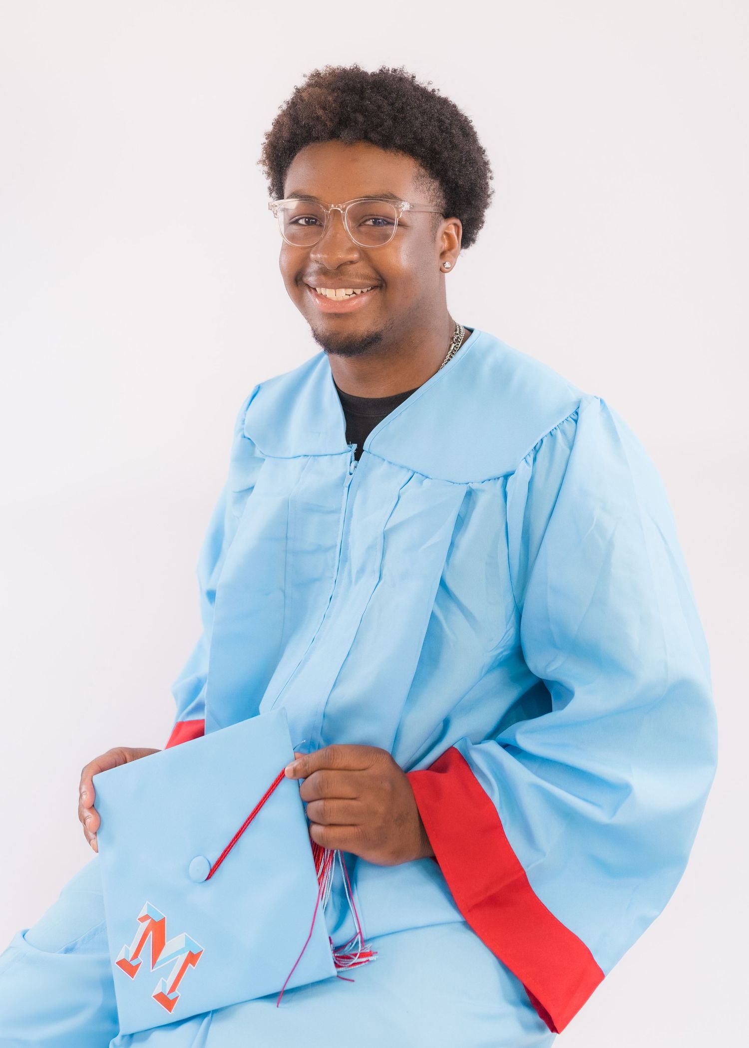 Graduate in light blue and red graduation regalia holding decorated cap against white background.