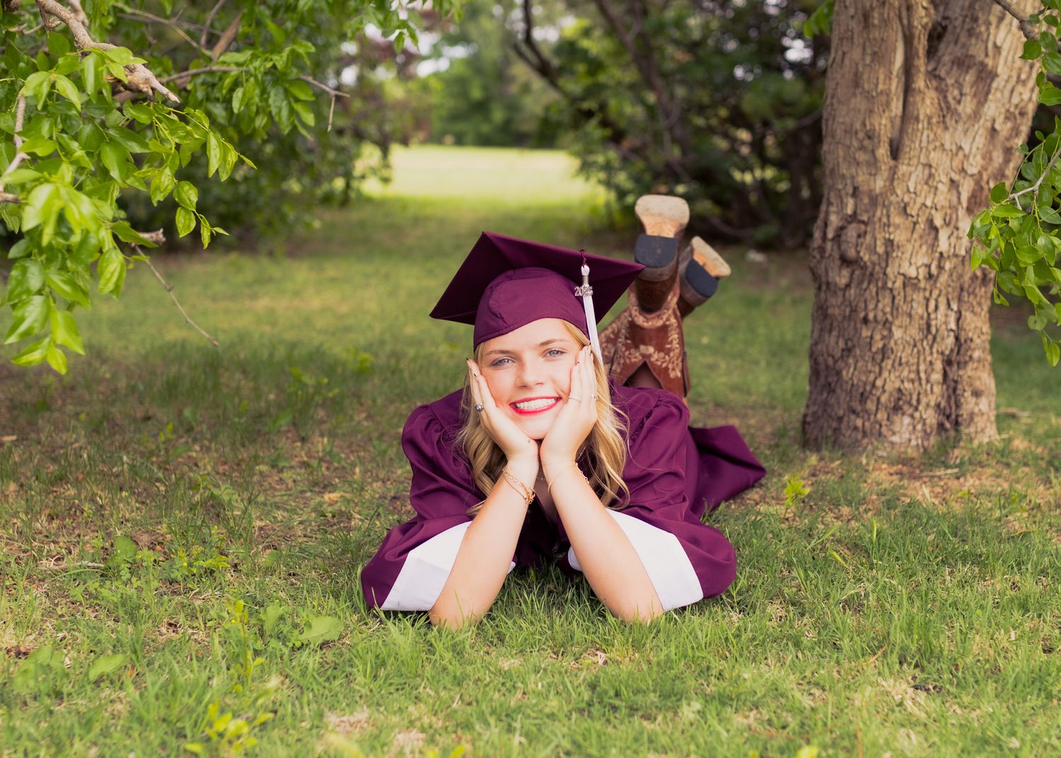 Graduate in purple cap and gown lying on grass for outdoor graduation photo.