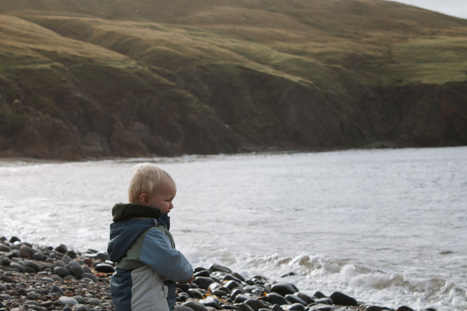 Person in warm clothing looking out over a rocky coastline.