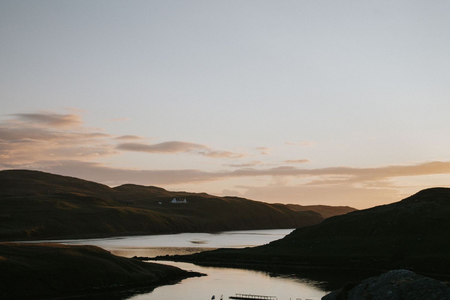 Sunset over a tranquil lake surrounded by rolling hills in silhouette.