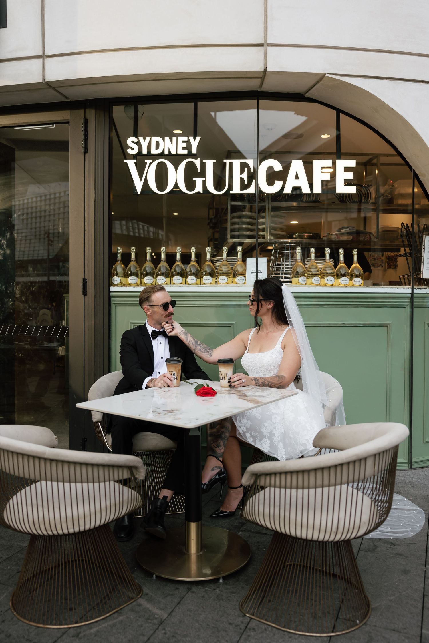 Bride and groom in sunglasses sitting together at outdoor table of Sydney Vogue Cafe sharing drinks after their elopement in Sydney CBD.