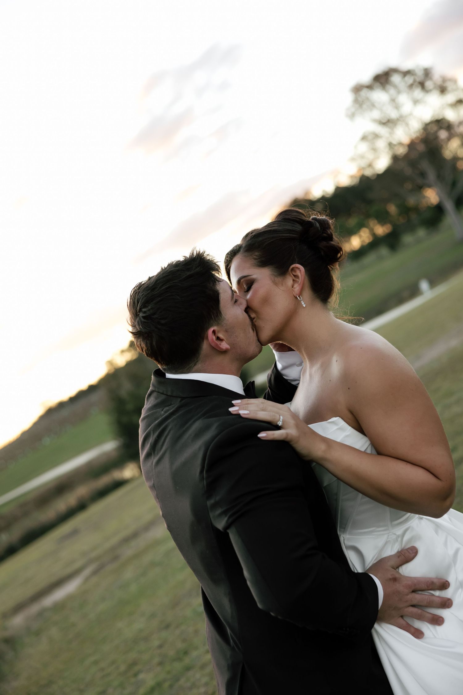 Bride and groom sharing a romantic kiss at sunset on their wedding day outdoors.