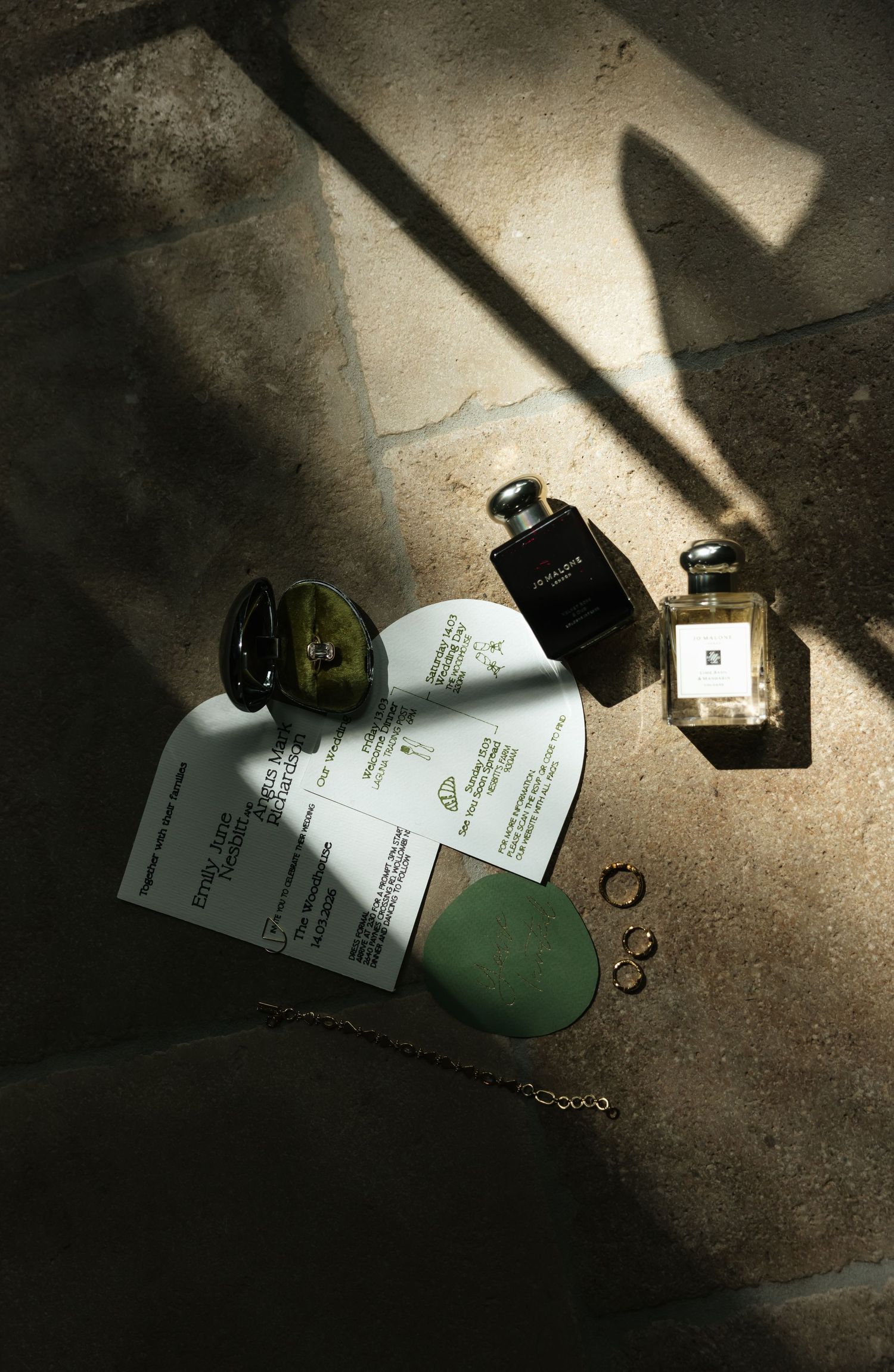 Flat lay of perfume bottles, rings, necklace and documents on stone surface with dramatic sunlight shadows at The Woodhouse, Wollombi.