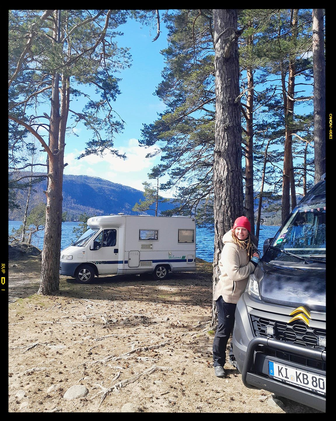 Snowy mountain camping scene with RV and pine trees along a scenic lakeside location in winter.