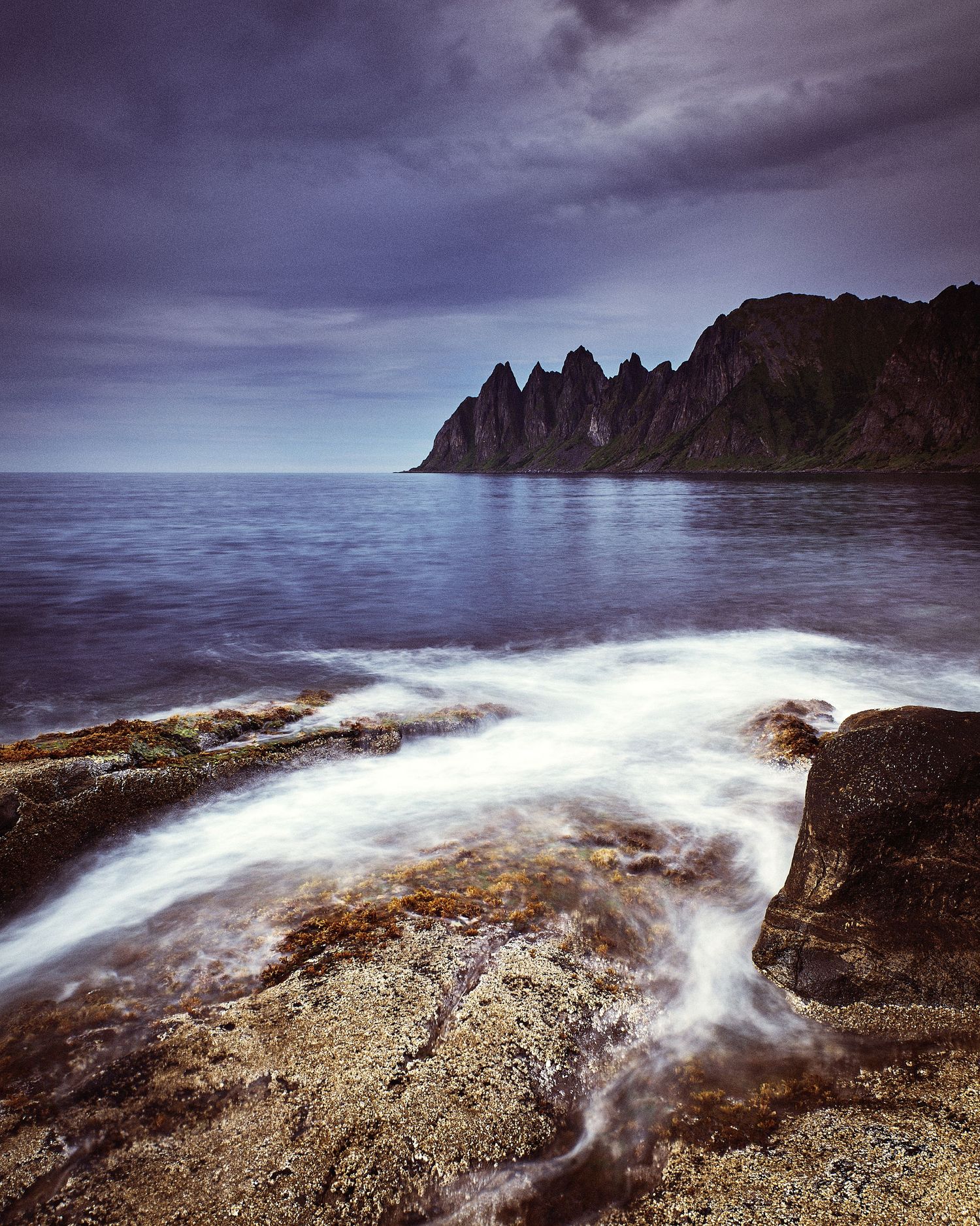 Moody seascape with crashing waves against rocky coast under stormy purple skies.