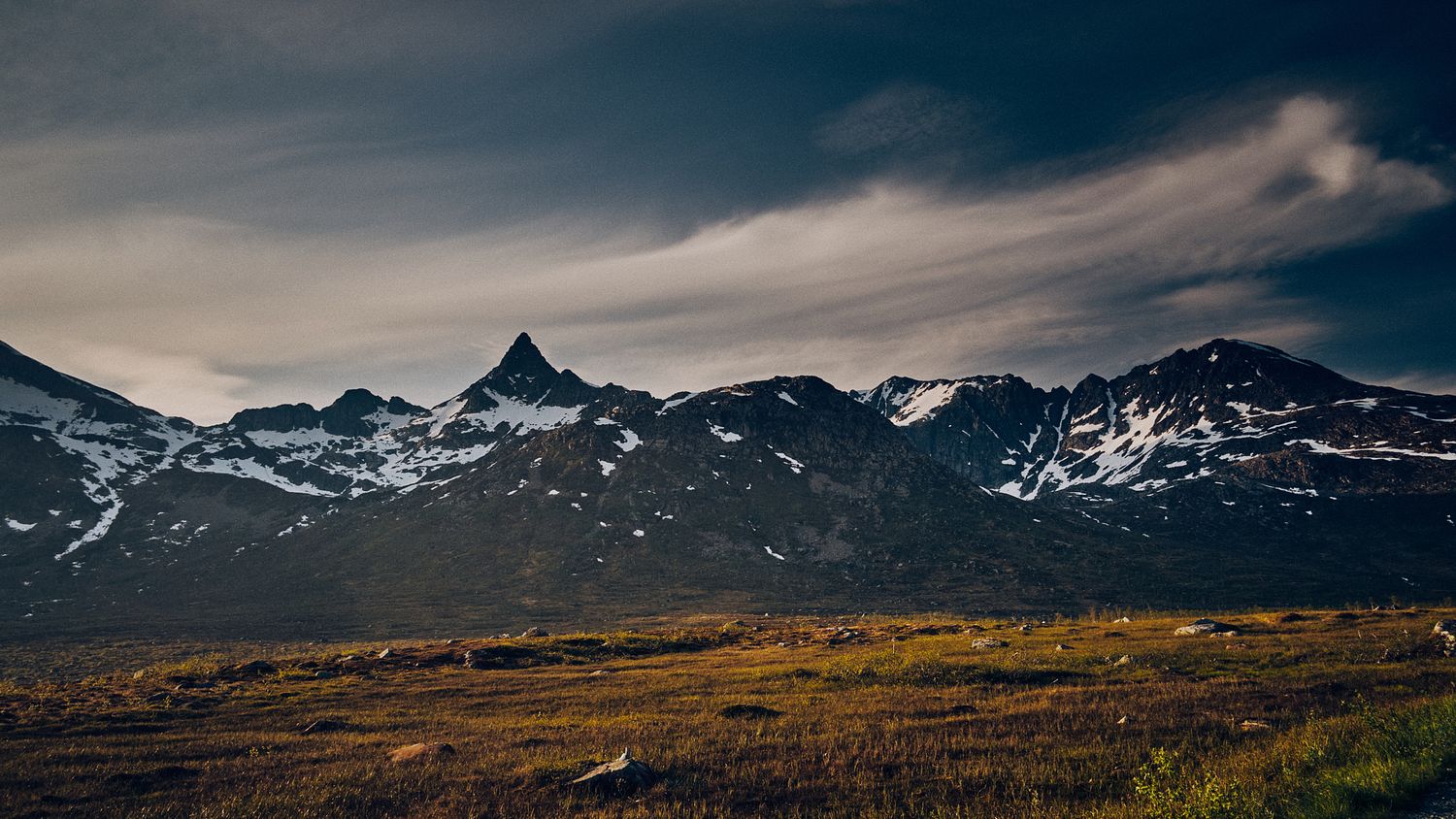 Dramatic mountain landscape with snow-capped peaks under moody sky in remote wilderness.
