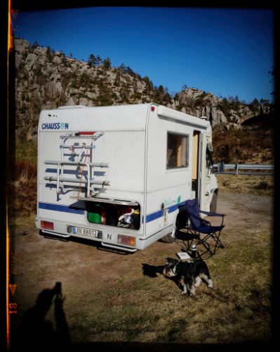 A white recreational vehicle parked in a scenic mountainous area with rocky cliffs in the background.