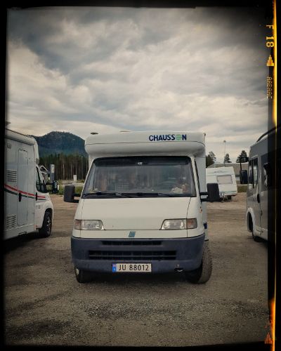 A white Chausson recreational vehicle parked in a campground with cloudy skies overhead.