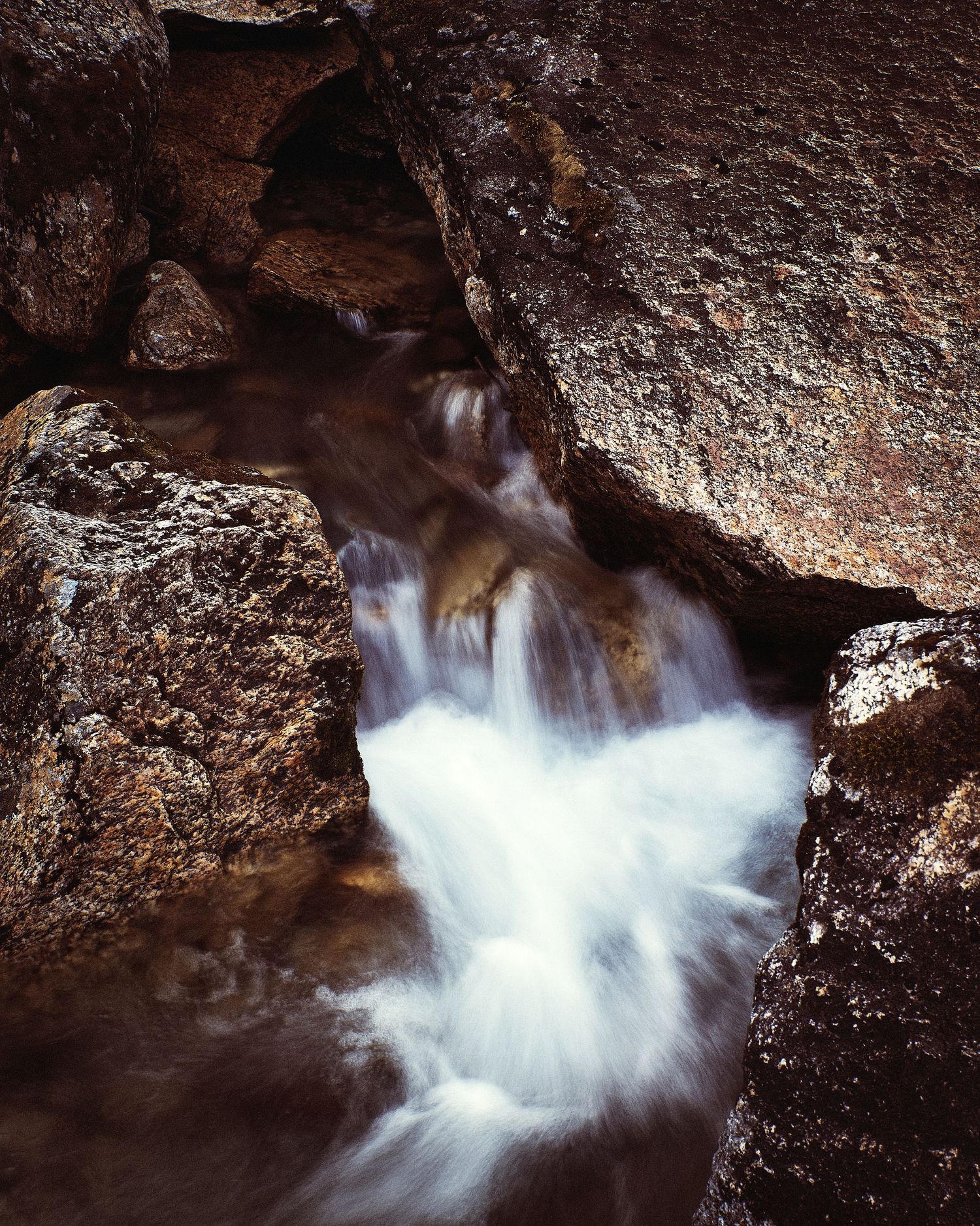 Dynamic waterfall rushing through rocky cave formation with white water spray.
