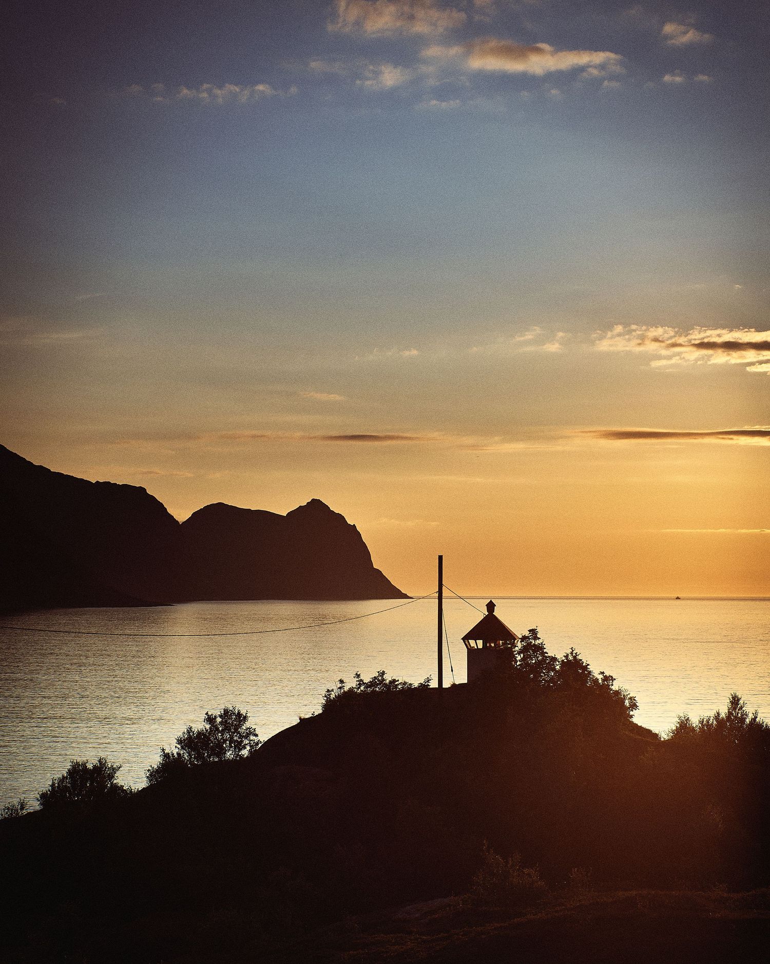 Silhouetted lighthouse on coastal cliff at sunset with golden sky over ocean.