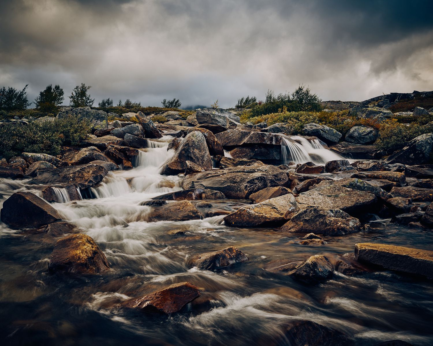 Rushing water cascades over rocky terrain in a dramatic panoramic waterfall landscape.