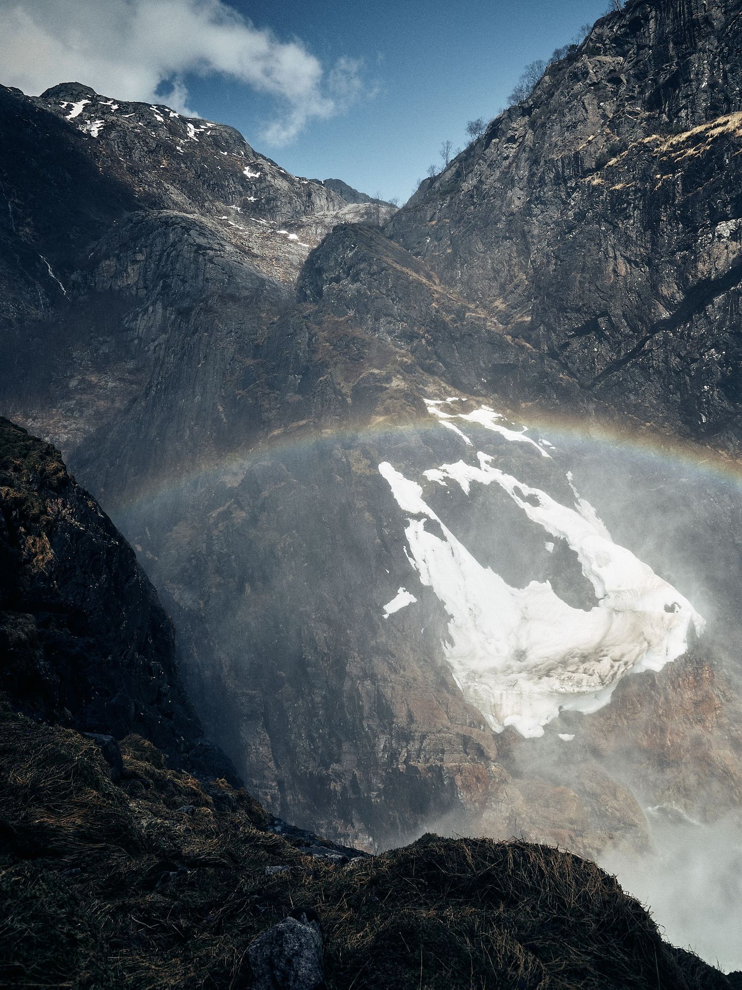 Snow-capped mountain peaks with dramatic rainbow forming in the mist of a cascading waterfall.