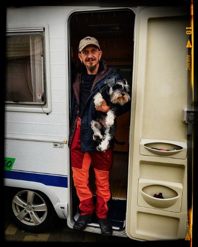 Someone stands in the doorway of a white camping trailer holding a black and white Schnauzer dog.