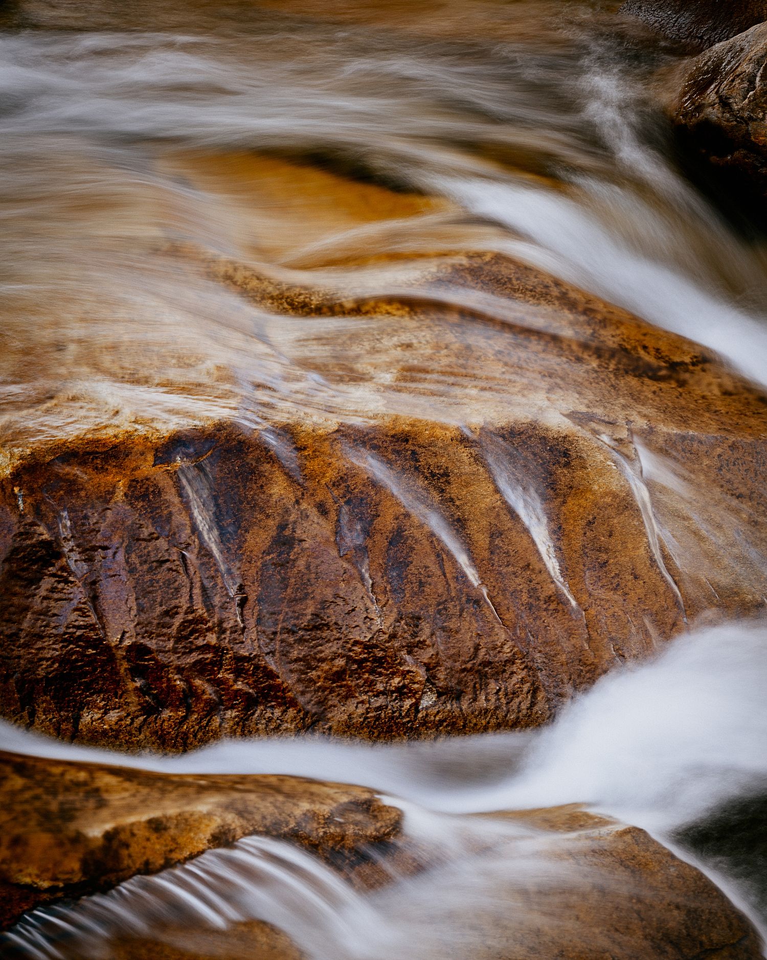 Long exposure shot of rushing water flowing over smooth orange-brown rocks creating silky white patterns.