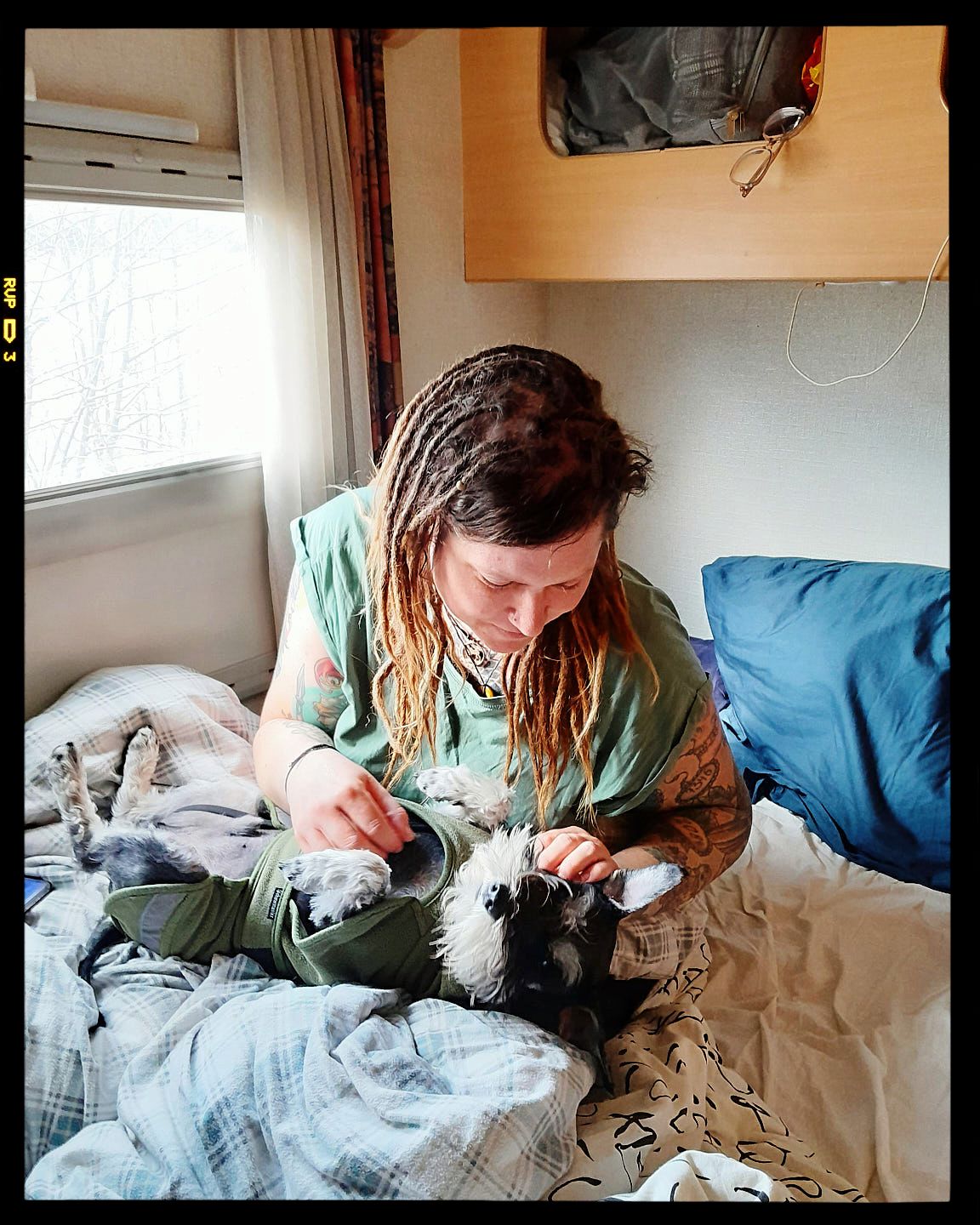Person with long hair in turquoise top comforts a black and white cat while relaxing on cozy bedding.