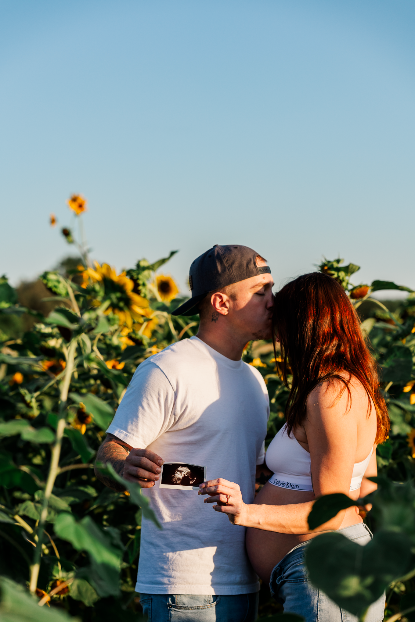 A couple shares an intimate moment in a sunflower field at golden hour.