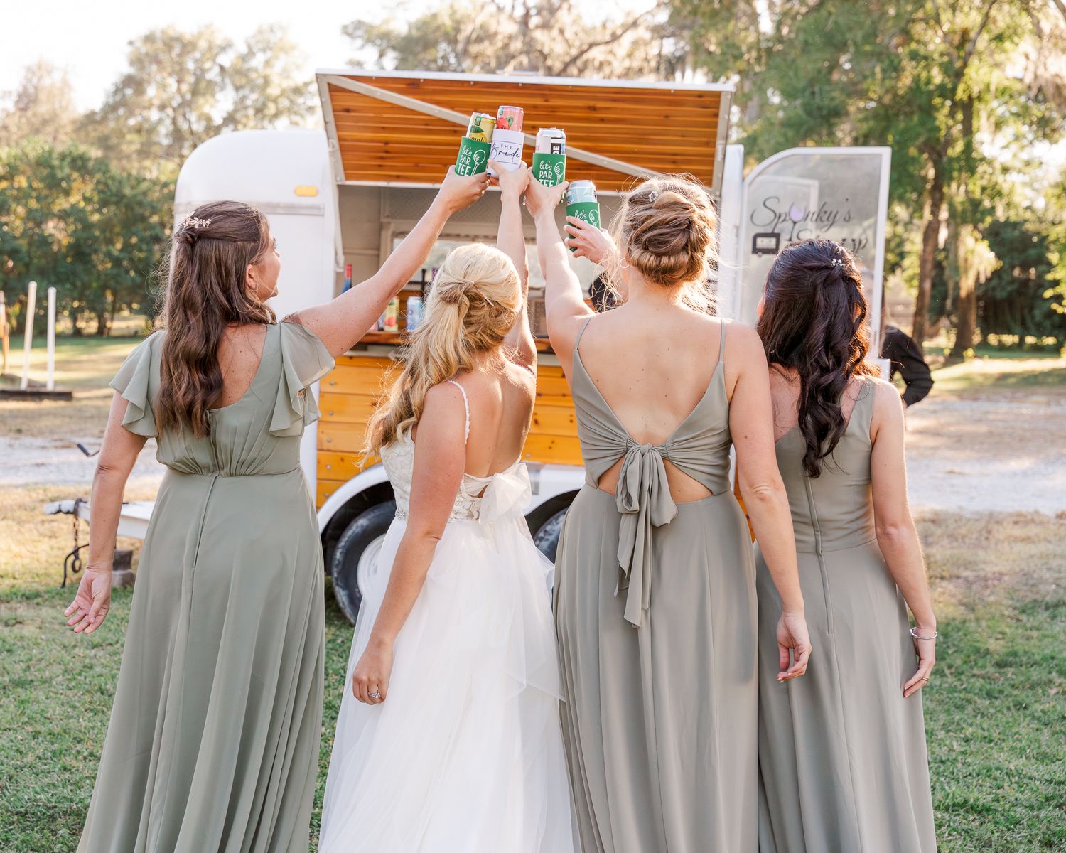 Bridesmaids in sage green dresses pose together outdoors at wedding.
