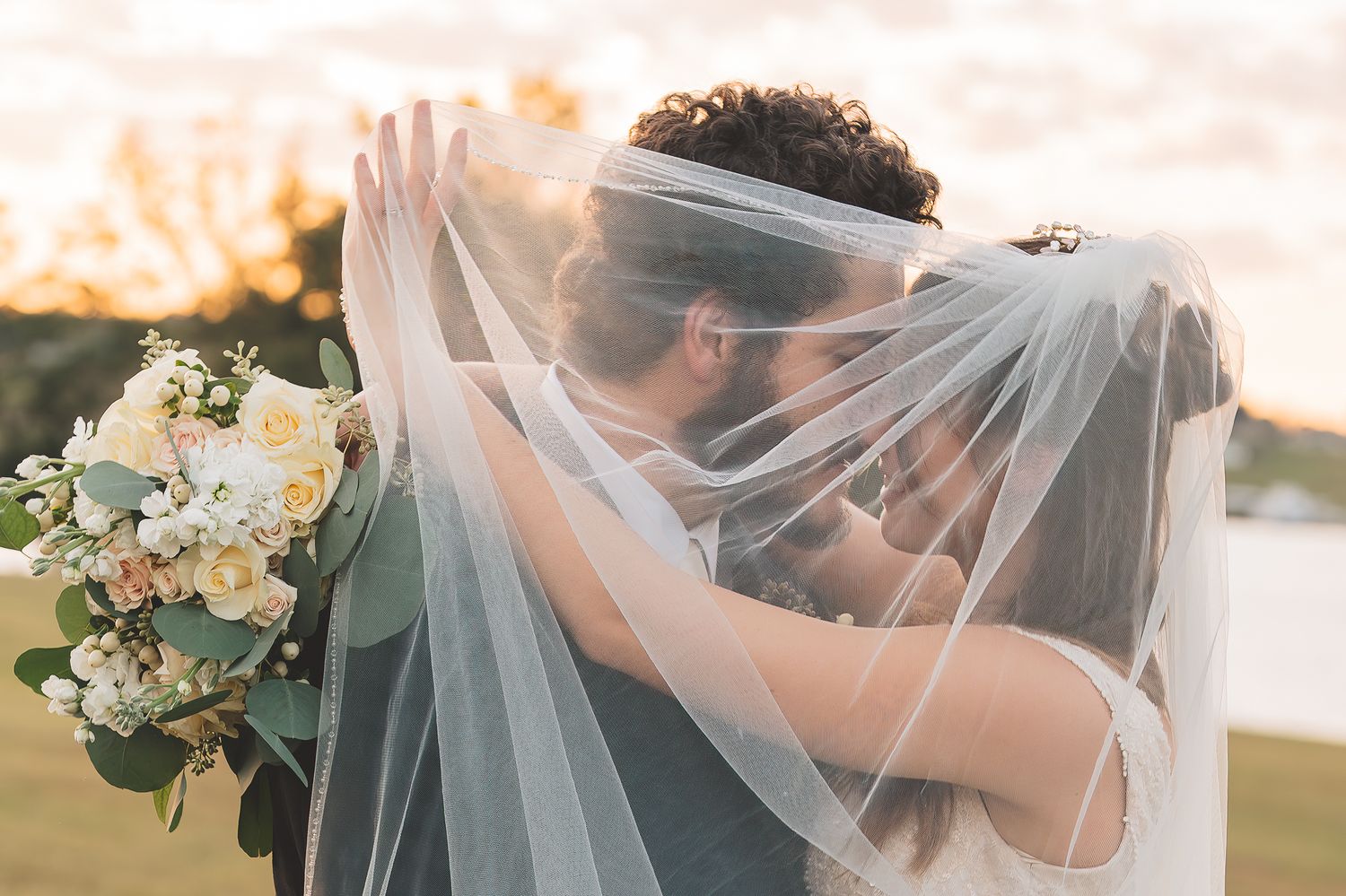 Romantic wedding photos showing couple embracing under a flowing white veil at sunset.