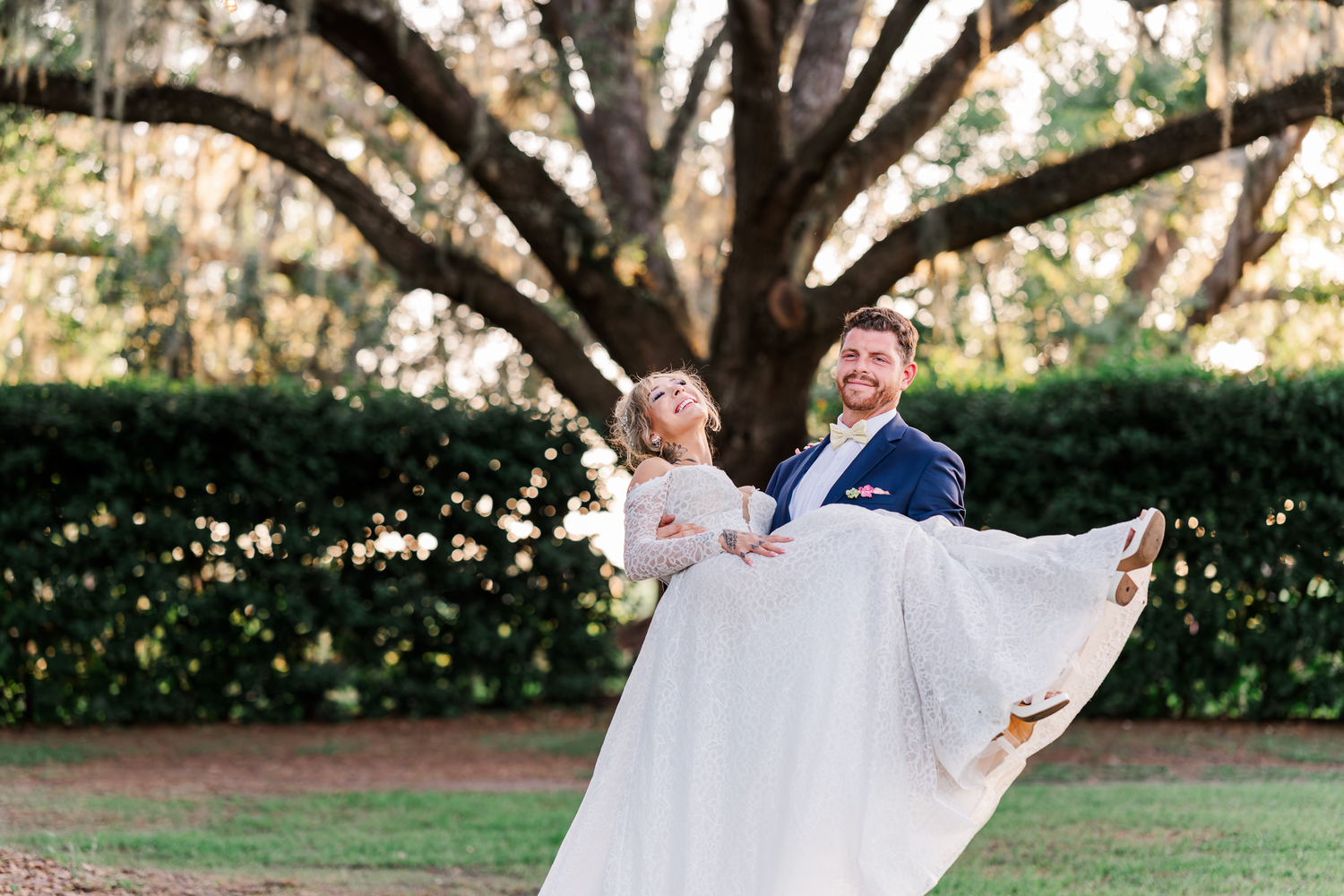 Joyful couple celebrates their wedding day under a grand oak tree draped with Spanish moss in a garden setting.