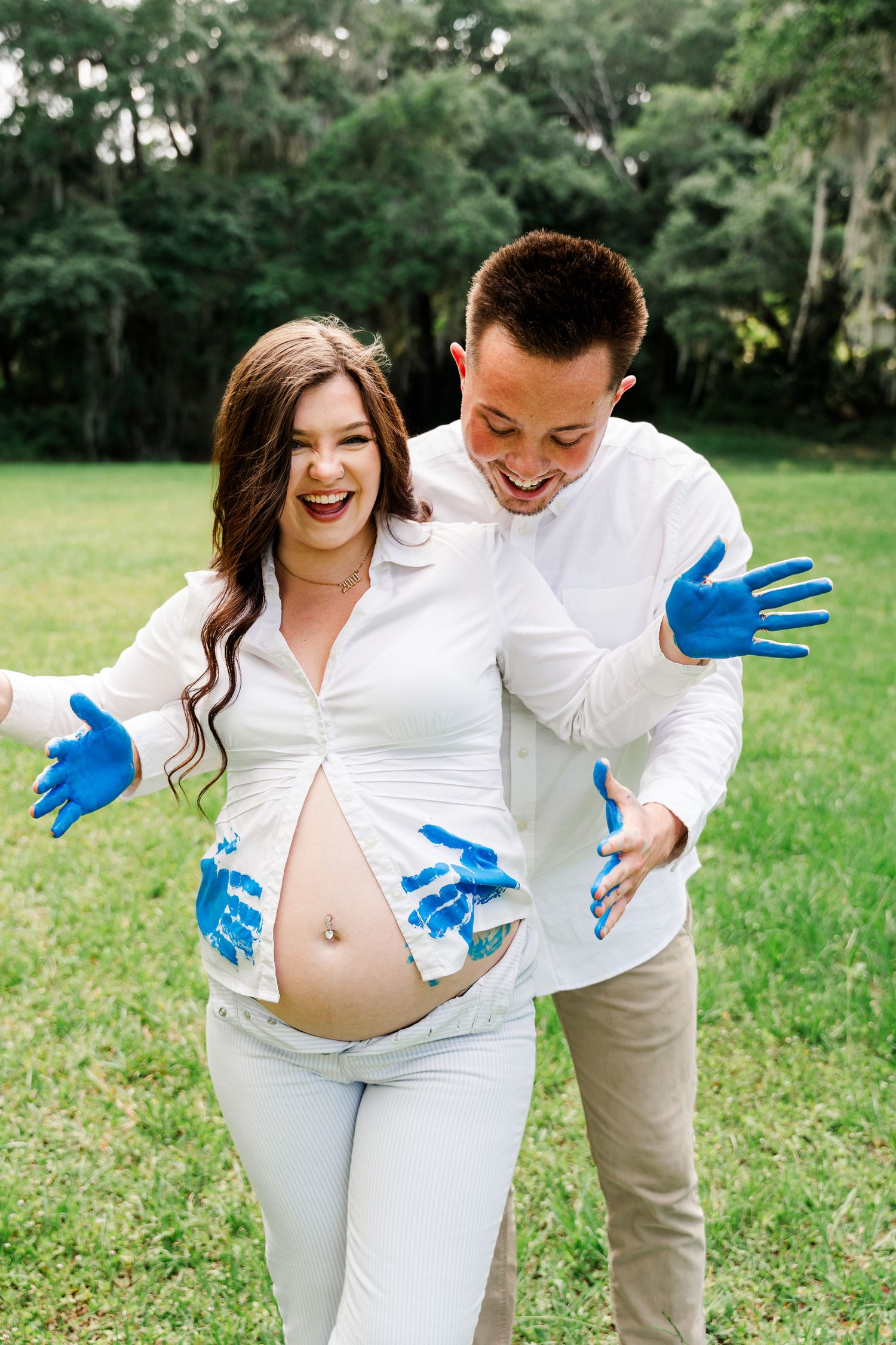 An expecting couple shares a joyful moment with blue handprints on their clothing and her bare belly.