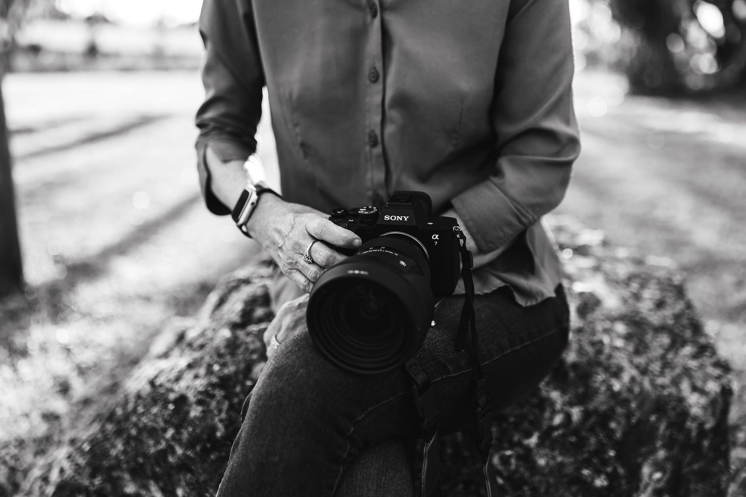 Black and white photo of Kathy holding a professional camera outdoors.