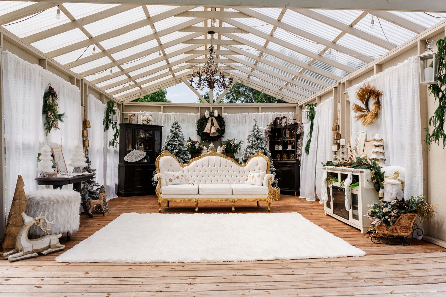 Interior view of an elegant white greenhouse wedding venue with rustic wood floors and enchanting string lights.