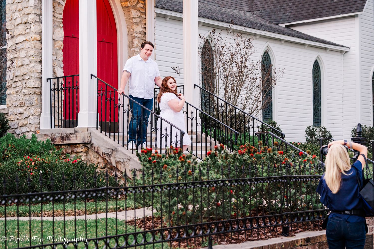 Behind the scenes of Kathy with her clients at a Historic white church exterior with red doors and iron fencing.