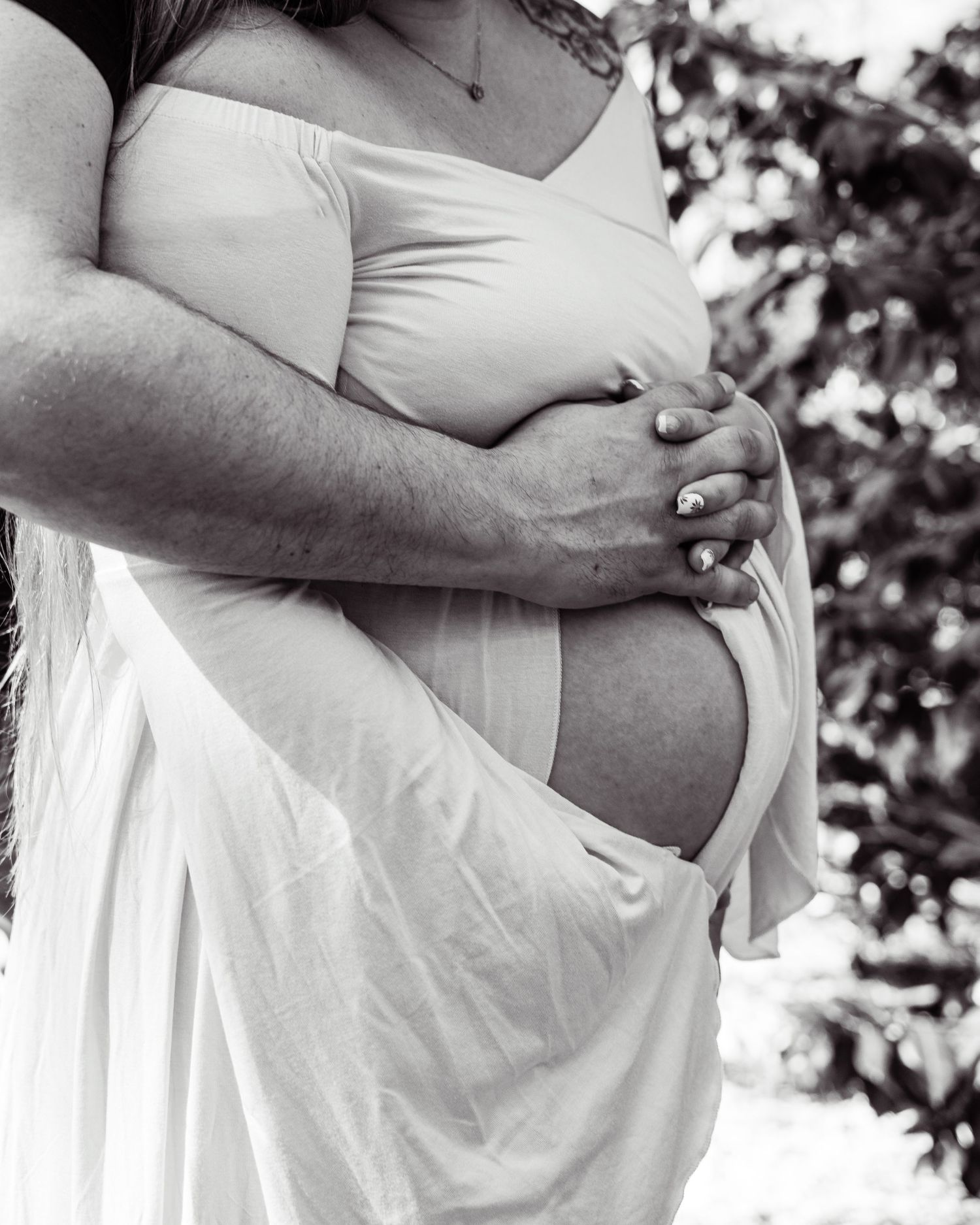 A black and white maternity photo showing hands cradling a pregnant belly in a flowing white dress.