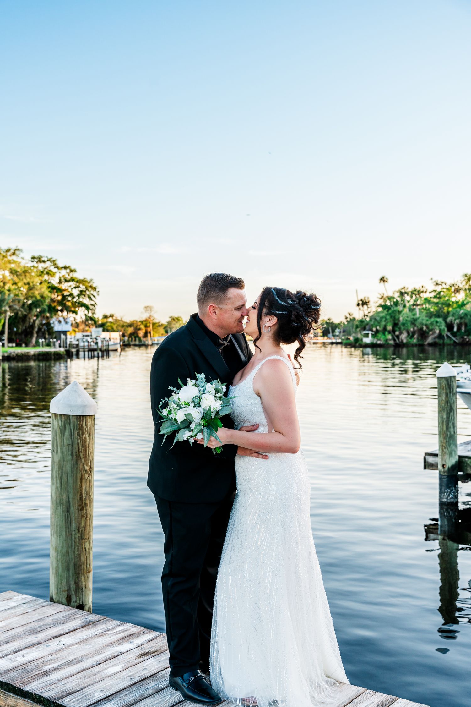A romantic couple shares intimate moments on a waterfront dock during a sunset wedding photoshoot.
