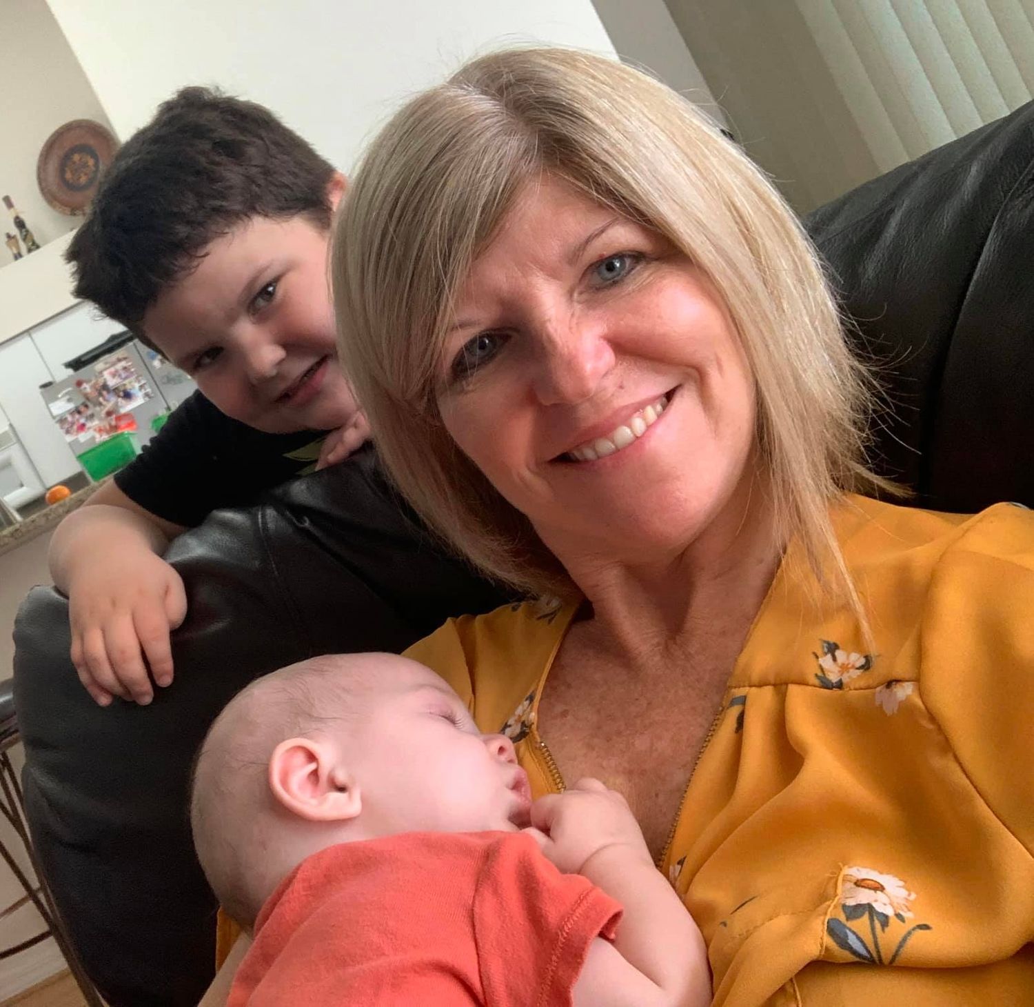 A family moment captured on a couch, featuring a sleeping baby and warm smiles in a cozy living room setting.