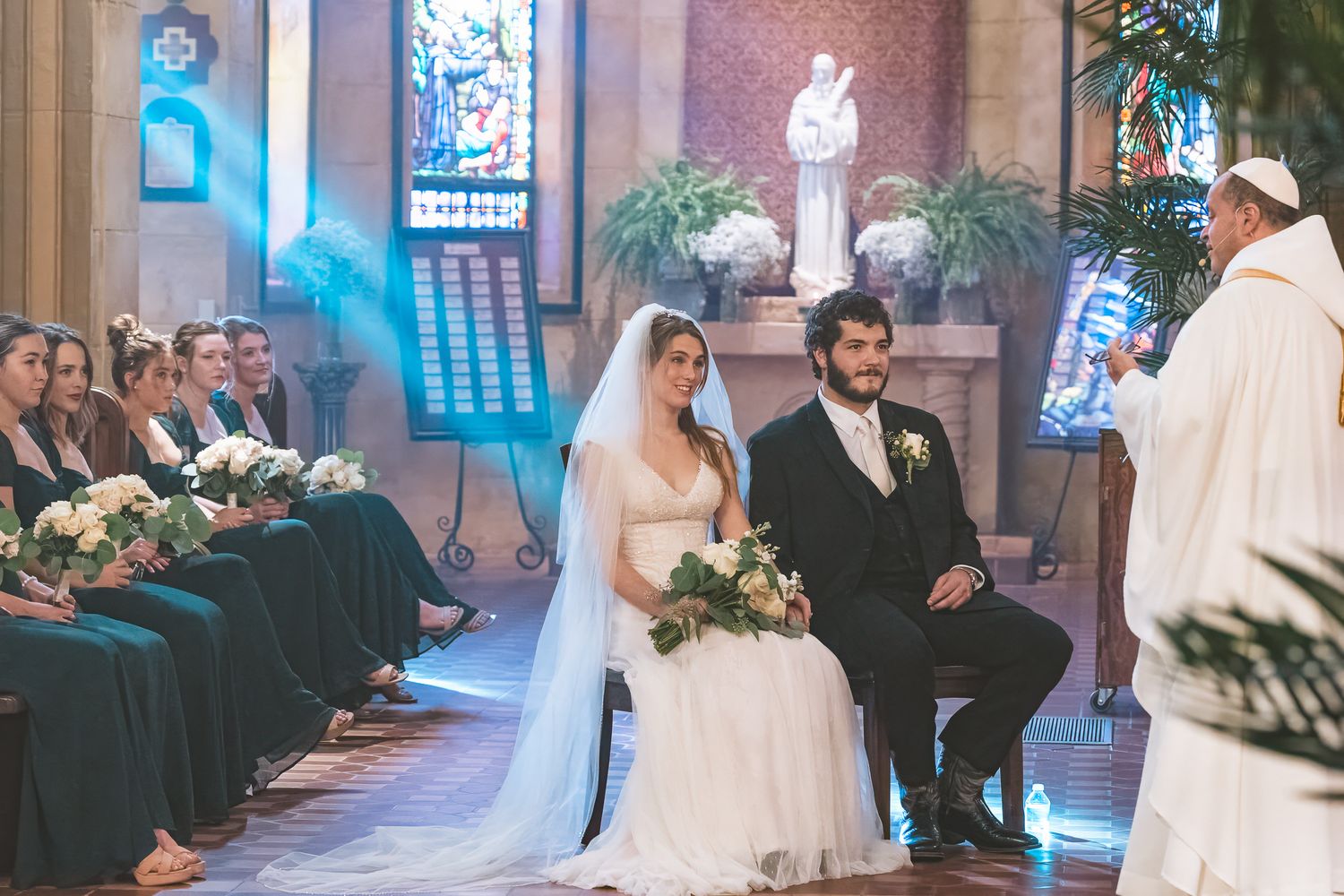 Indoor wedding ceremony with dramatic blue lighting in a brick-walled chapel setting.
