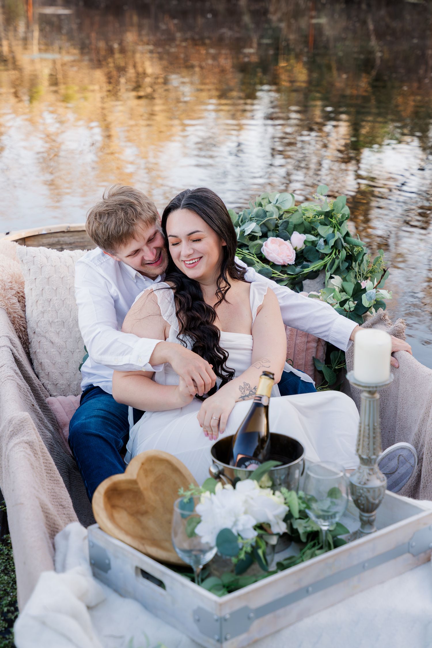 Romantic couple shares intimate moments in a white vintage boat decorated with flowers and candles by the water.