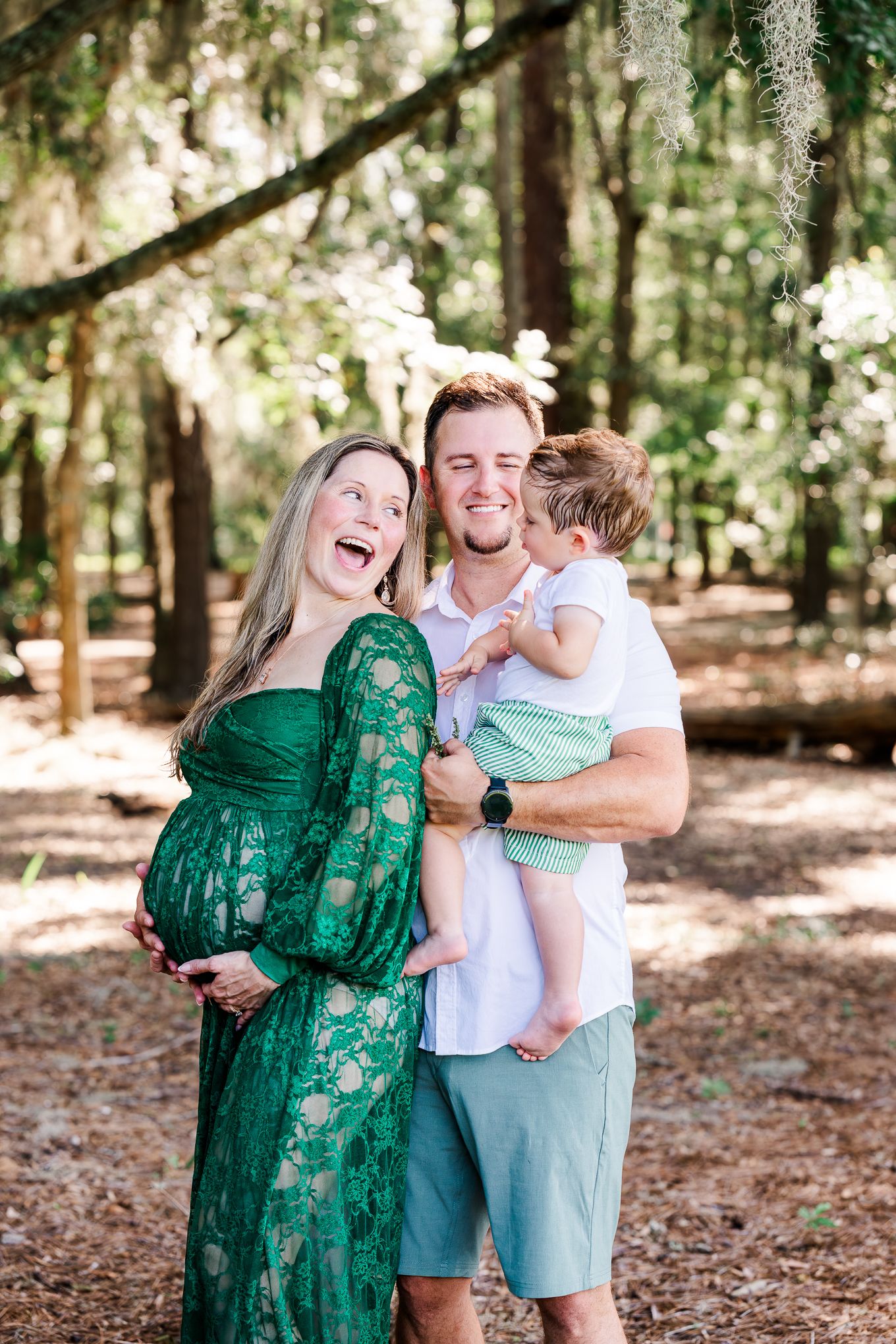 A loving family shares joyful moments together in a sunlit forest setting wearing coordinated green and blue outfits.