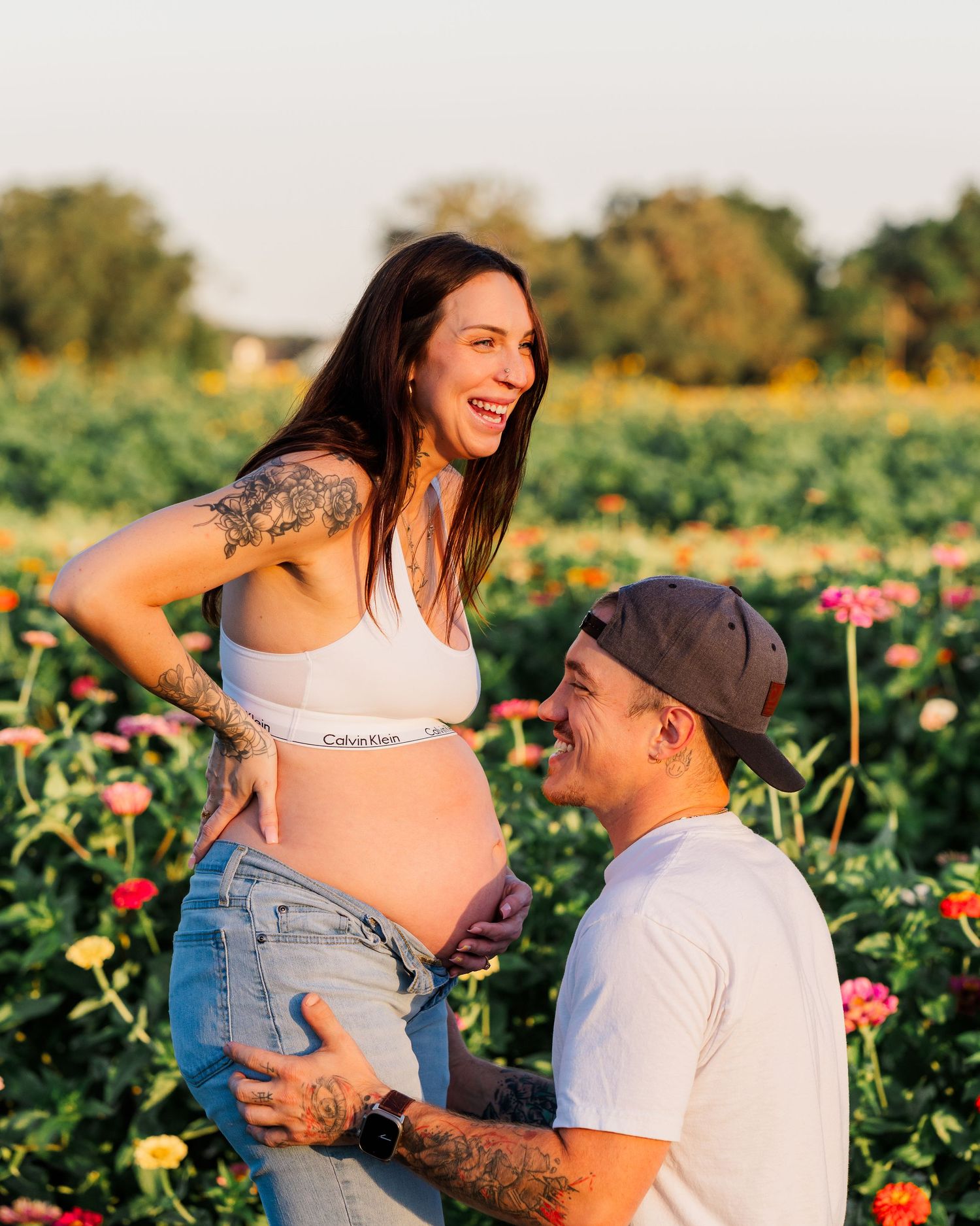 Couple shares tender moment in a blooming flower garden during sunset maternity photoshoot.