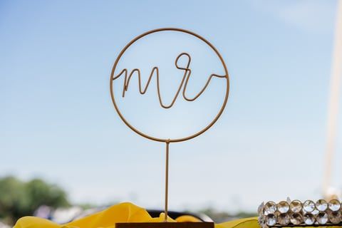 A minimalist gold 'mr' wire script decoration tops a table against a blue sky background.