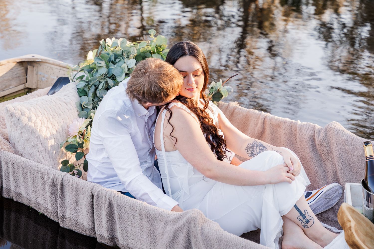 A romantic couple in wedding attire shares tender moments by a scenic waterfront setting at sunset.