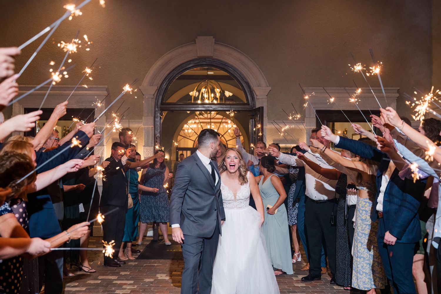 Wedding couple exit under sparkler arch with guests lining pathway.