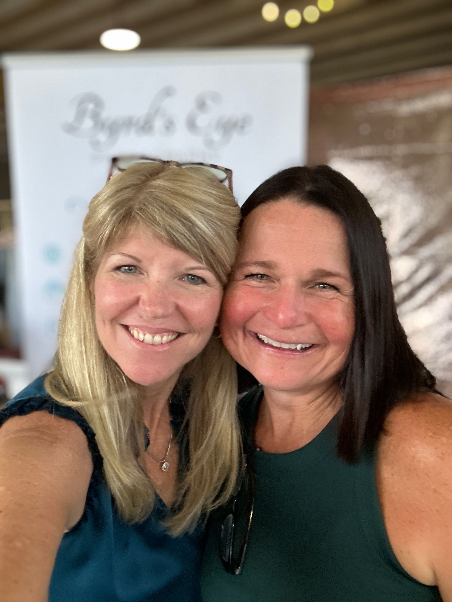 Indoor selfie with two people smiling warmly against blurred background.