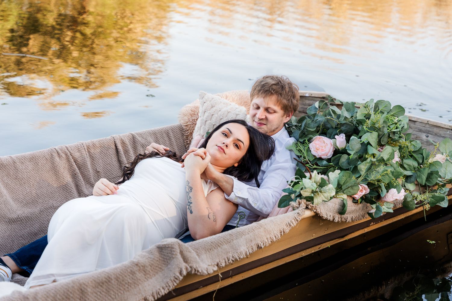 A couple in a rustic wooden boat with floral decorations on a  lake with golden reflections at the Gathering Table Venue Plant City, Florida