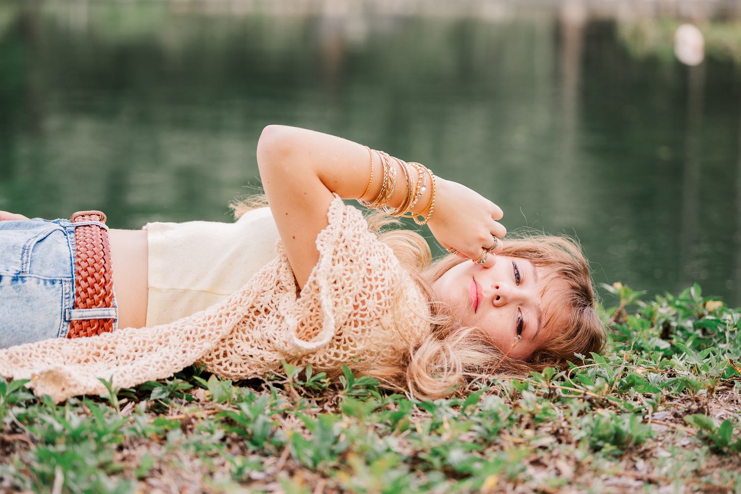 Dreamy portrait session with subject laying in grass beside reflective pond.