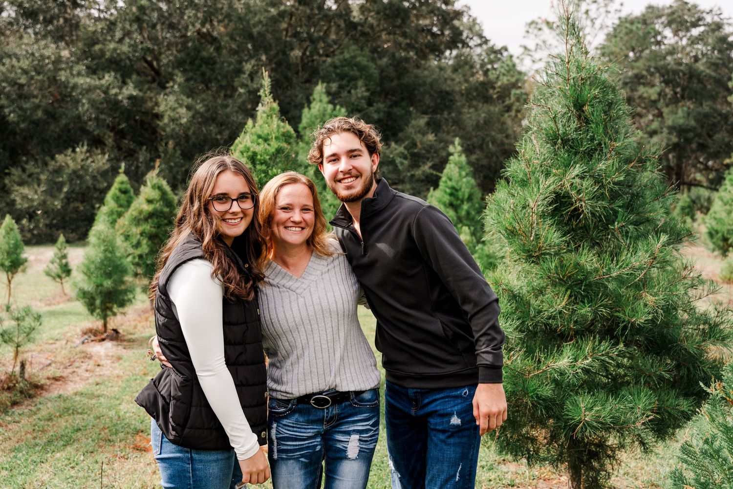 Family poses together outdoors at a Christmas tree farm on a bright autumn day.