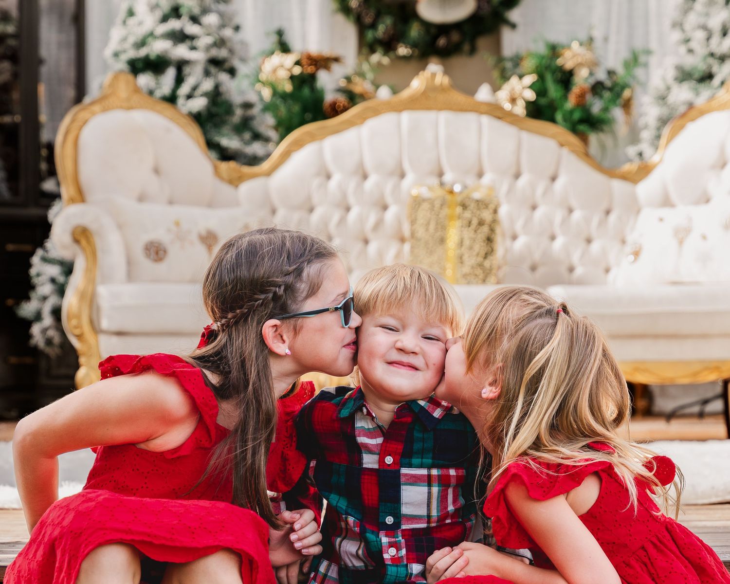 Children in red and plaid holiday outfits playing together in an elegant white room setting.