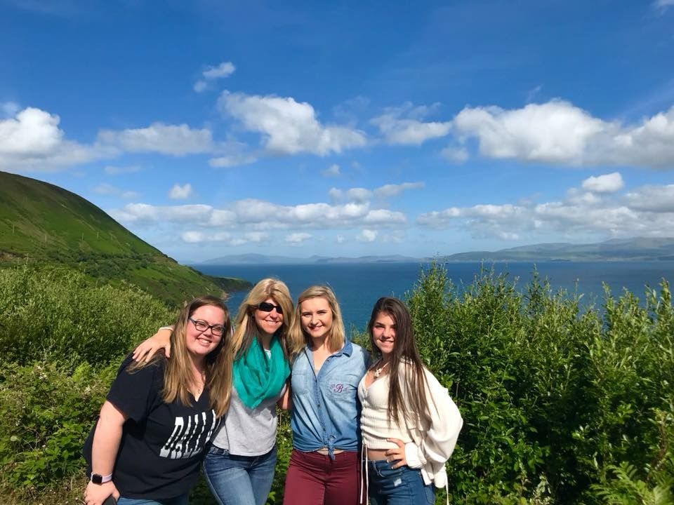 Group photo on a scenic coastal hillside in Ireland with blue ocean and sky in background.