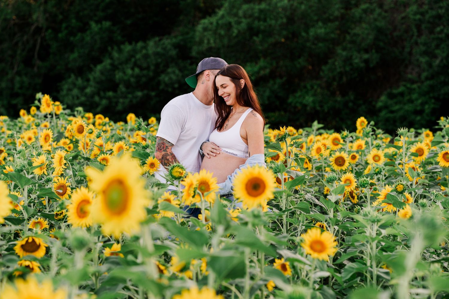 A romantic couple shares tender moments while walking through a vibrant yellow sunflower field on a summer day.